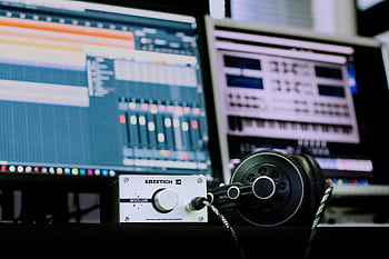 Close-up of a professional music studio setup featuring an amplifier and heads with digital audio workstations in the background. HD wallpaper