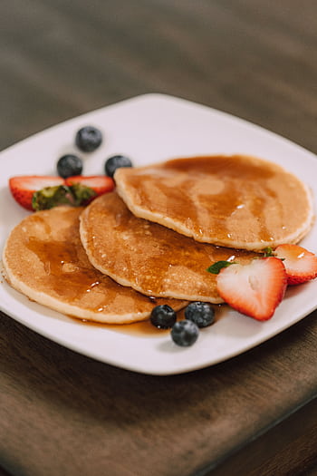 Mouth-watering pancakes served with fresh strawberries, blueberries, and syrup on a white plate. HD phone wallpaper