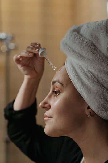 Close-up side view of a woman applying skincare serum with a dropper, promoting beauty routine. HD phone wallpaper