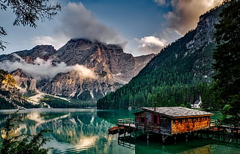 Peaceful mountain lake scene featuring a rustic boathouse and stunning reflections. HD wallpaper