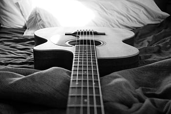 Monochrome of an acoustic guitar resting on a bed, capturing musical essence. HD wallpaper