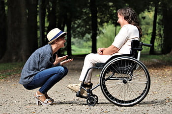 Two women enjoy a lively conversation in a sunny park, embracing friendship and happiness. HD wallpaper