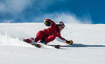 A skier in vibrant red gear skillfully navigates a snowy slope on a sunny day. HD wallpaper