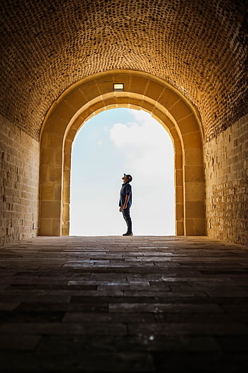 Man silhouetted in ancient stone archway exploring the historic architecture. HD phone wallpaper