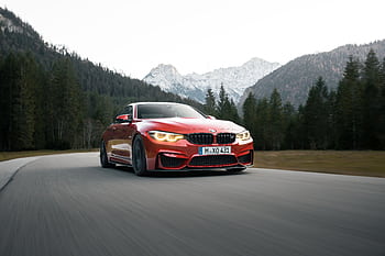 A stunning red BMW car speeds along a forest road with majestic mountains in the background. HD wallpaper
