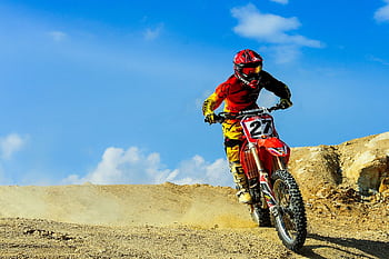 Motocross racer speeding through a dusty track under blue skies. Action-packed outdoor sport. HD wallpaper