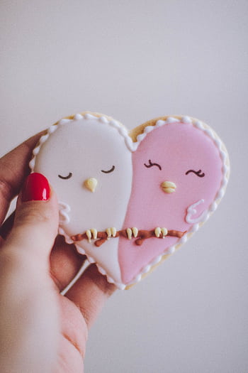 Heart-shaped cookie with bird design held by a hand, perfect dessert symbolizing love. HD phone wallpaper