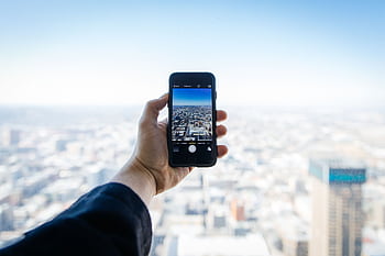 A hand holding a smart capturing an urban cityscape from above. HD wallpaper
