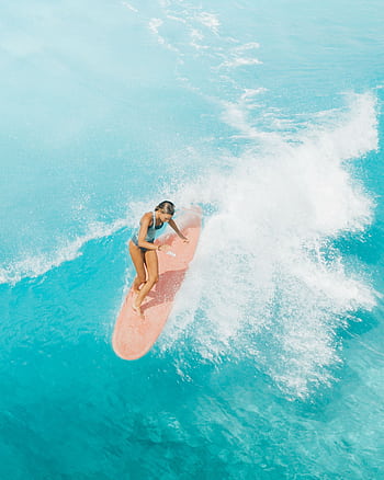 Aerial view of a female surfer skillfully riding waves on a vibrant turquoise ocean. HD phone wallpaper