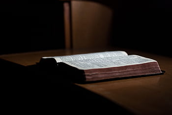 A dimly lit open Bible rests on a wooden table, inviting reflection and study. HD wallpaper