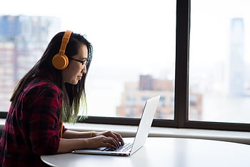 Asian woman with heads using laptop for remote work in a city setting. HD wallpaper