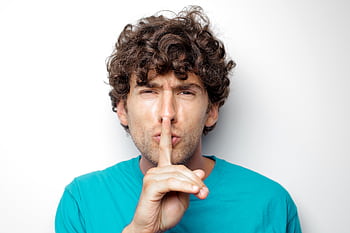 Adult man with curly hair in blue shirt making a silence gesture on white background. HD wallpaper