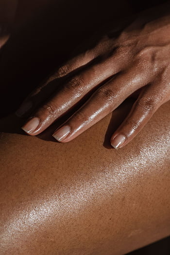 A detailed close-up of a woman's hand resting gently on her leg, highlighted by warm sunlight, showcasing skin texture and natural beauty. HD phone wallpaper
