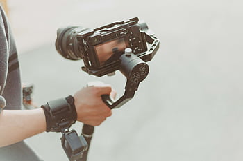 Close-up of a videographer holding a modern camera with stabilizer outdoors. Capturing high-quality footage. HD wallpaper