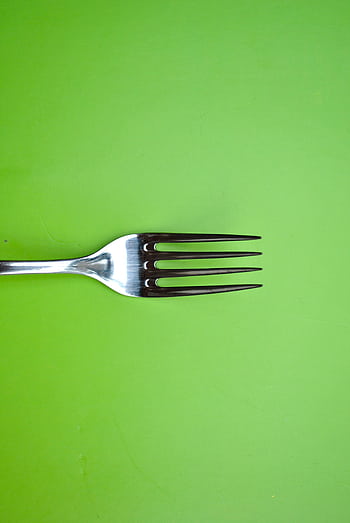 A simple arrangement of a stainless steel fork on a bright green surface, showcasing minimalist art. HD phone wallpaper