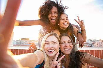 Cheerful friends capturing a fun selfie on a rooftop during sunset, enjoying a positive and trendy moment. HD wallpaper