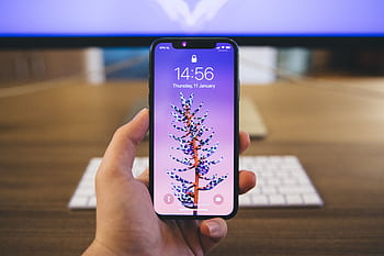 Close-up of a hand holding a smart with a vibrant purple screen displaying the time and date. HD wallpaper