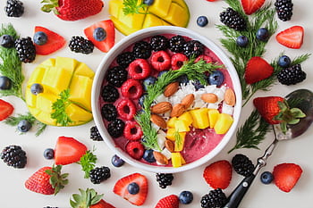 A vibrant, healthy fruit smoothie bowl topped with fresh berries, mango, and almonds. HD wallpaper