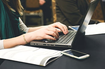 Adult woman typing on a laptop at a desk with a smart and documents. HD wallpaper