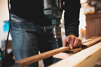 Close-up of a person using an electric drill on a wooden plank, showcasing detailed woodworking skills. HD wallpaper