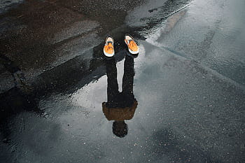 Reflection of legs and shoes in a puddle on a wet street, creating a surreal urban scene. HD wallpaper