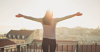 A woman stands with outstretched arms on a sunny balcony, embracing the morning light. HD wallpaper