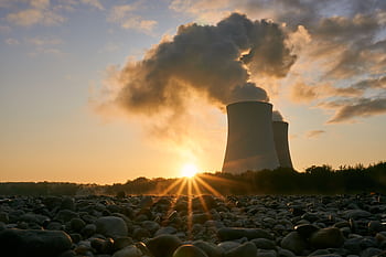 A nuclear power plant emitting steam at sunrise, creating a dramatic skyline with visible air pollution. HD wallpaper