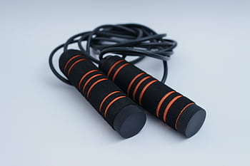 A minimalist close-up of black and orange exercise skipping rope on a clean white background. HD wallpaper
