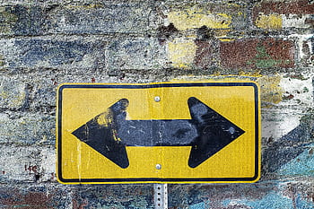Weathered yellow two-way street sign on a textured rustic brick wall. Urban art style. HD wallpaper