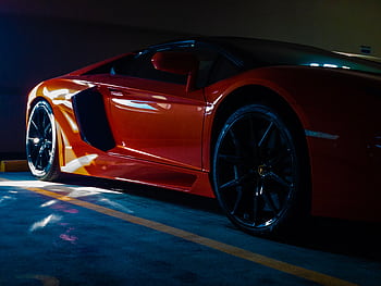 Close-up of a vibrant orange sports car parked in a sunlit garage, showcasing luxury and modern design. HD wallpaper