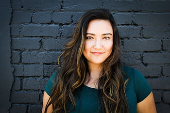 A captivating portrait of a woman smiling confidently in front of a brick wall, showcasing her long brunette hair and vibrant eyes. HD wallpaper