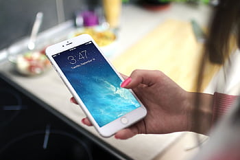 Close-up shot of a person holding a smart in a kitchen setting, displaying the lock screen. HD wallpaper