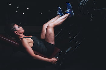 Focused woman doing leg press exercise in a dimly lit gym. HD wallpaper