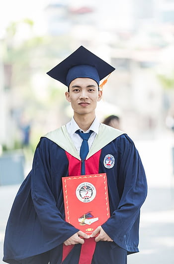 Proud graduate in academic gown holding diploma, celebrating academic success. HD phone wallpaper