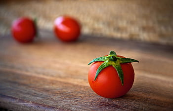 Vibrant cherry tomatoes resting on a rustic wooden surface, showcasing freshness and organic appeal. HD wallpaper
