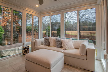 Spacious sunroom with contemporary sofa and large windows offering a serene outdoor view. HD wallpaper