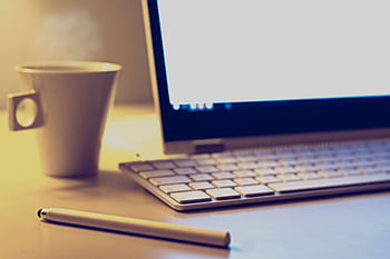 Cozy office setup with a laptop, keyboard, pen, and coffee cup on a desk. HD wallpaper