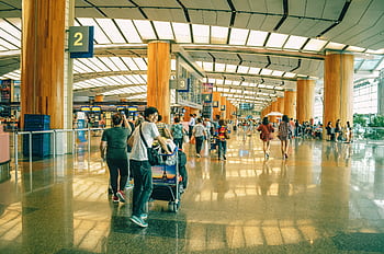 Travelers bustling through Singapore Changi Airport terminal, highlighting the dynamic and vibrant atmosphere of international travel. HD wallpaper