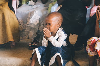 A young child in Tanzania prays in contemplation during a community gathering, symbolizing faith and innocence. HD wallpaper