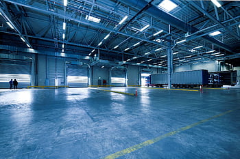 Wide view of an empty modern warehouse with industrial lighting and trucks. HD wallpaper