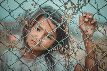 A thoughtful child gazes through a wire fence, symbolizing innocence and curiosity. HD wallpaper