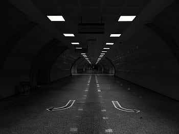 A dark, atmospheric view of an empty underground tunnel in grayscale. HD wallpaper