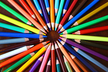 Vibrant spiral of colored pencils forming a rainbow spectrum on a wooden desk. HD wallpaper