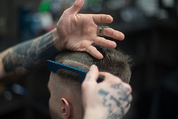 Close-up of a tattooed barber giving a stylish haircut indoors, highlighting modern grooming techniques. HD wallpaper