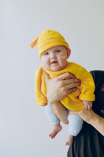 Cute baby in a yellow outfit being held indoors against a light background. HD phone wallpaper