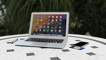 Open laptop with app icons displayed, smart and pen on white table outdoors. HD wallpaper