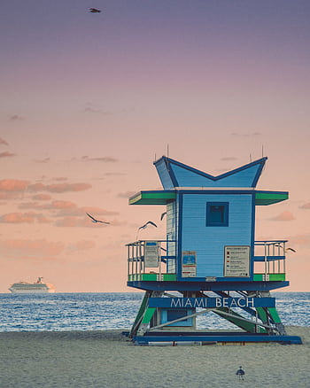 A tranquil scene of Miami Beach at sunset featuring a colorful lifeguard tower and a serene ocean view. HD phone wallpaper