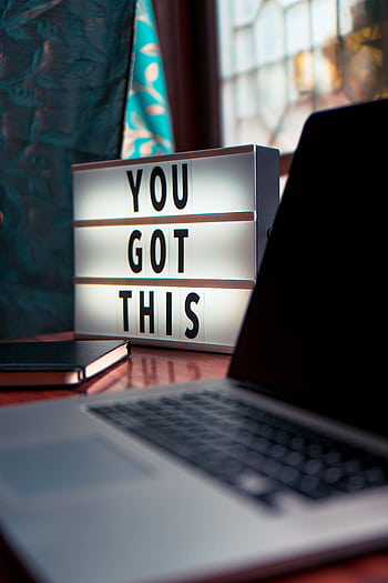 Illuminated lightbox with a motivational quote beside a laptop, promoting productivity. HD phone wallpaper