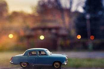 A vintage blue toy car with a blurred city background, graphed outdoors at twilight. HD wallpaper