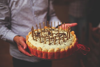 Close-up of a decorated birtay cake with lit candles held by a person at a celebration. HD wallpaper
